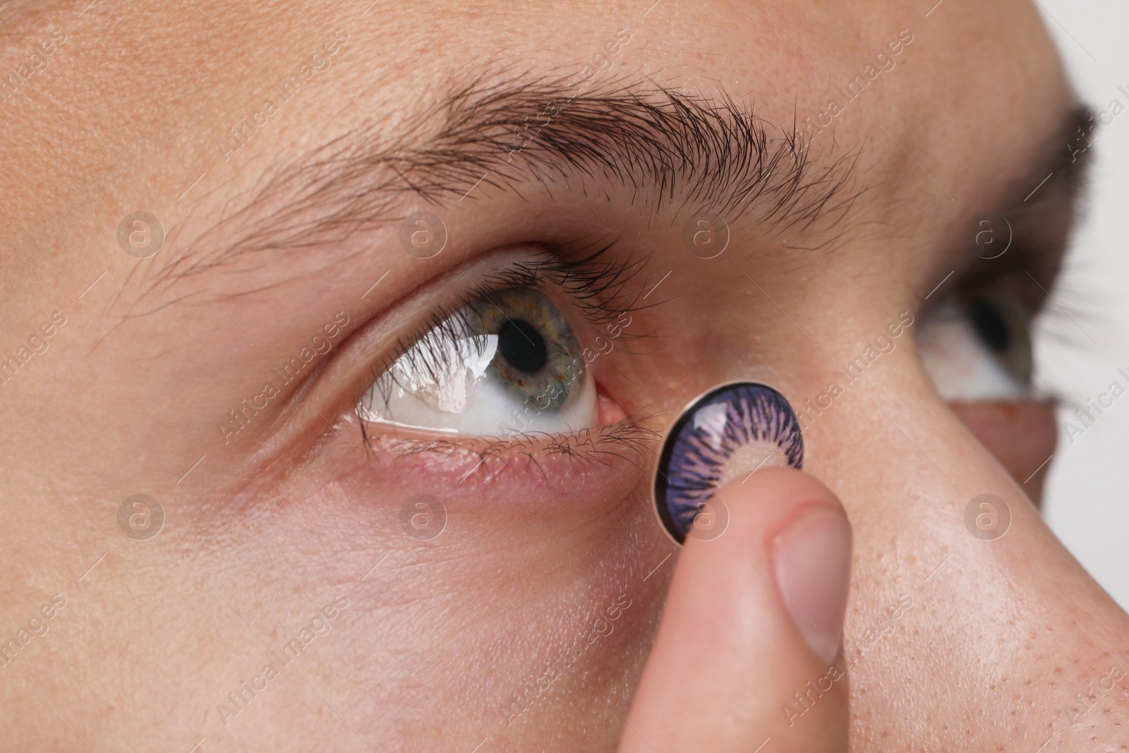 Photo of Man putting color contact lens in his eye, closeup