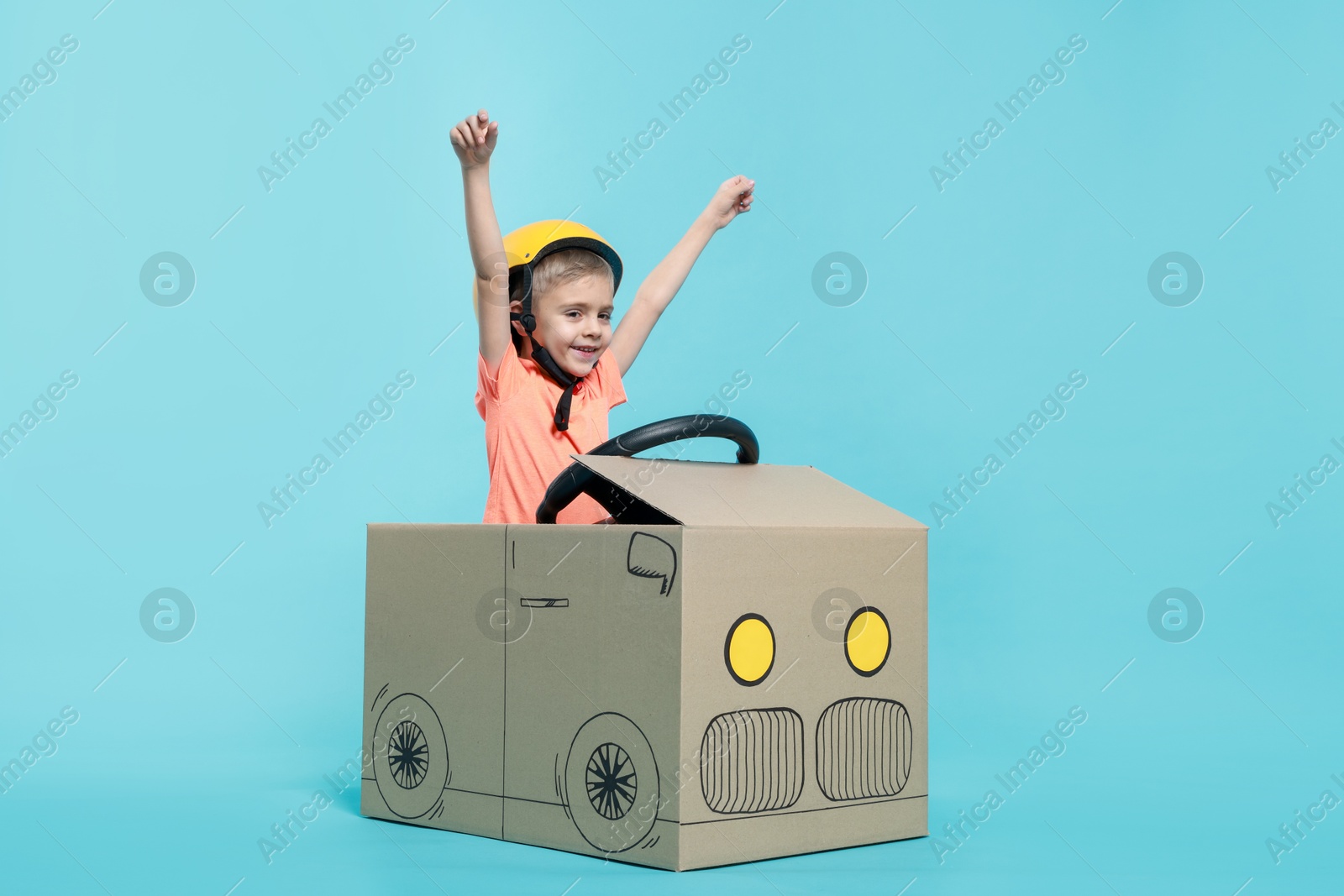 Photo of Little boy driving car made of cardboard on light blue background