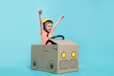 Photo of Little boy driving car made of cardboard on light blue background