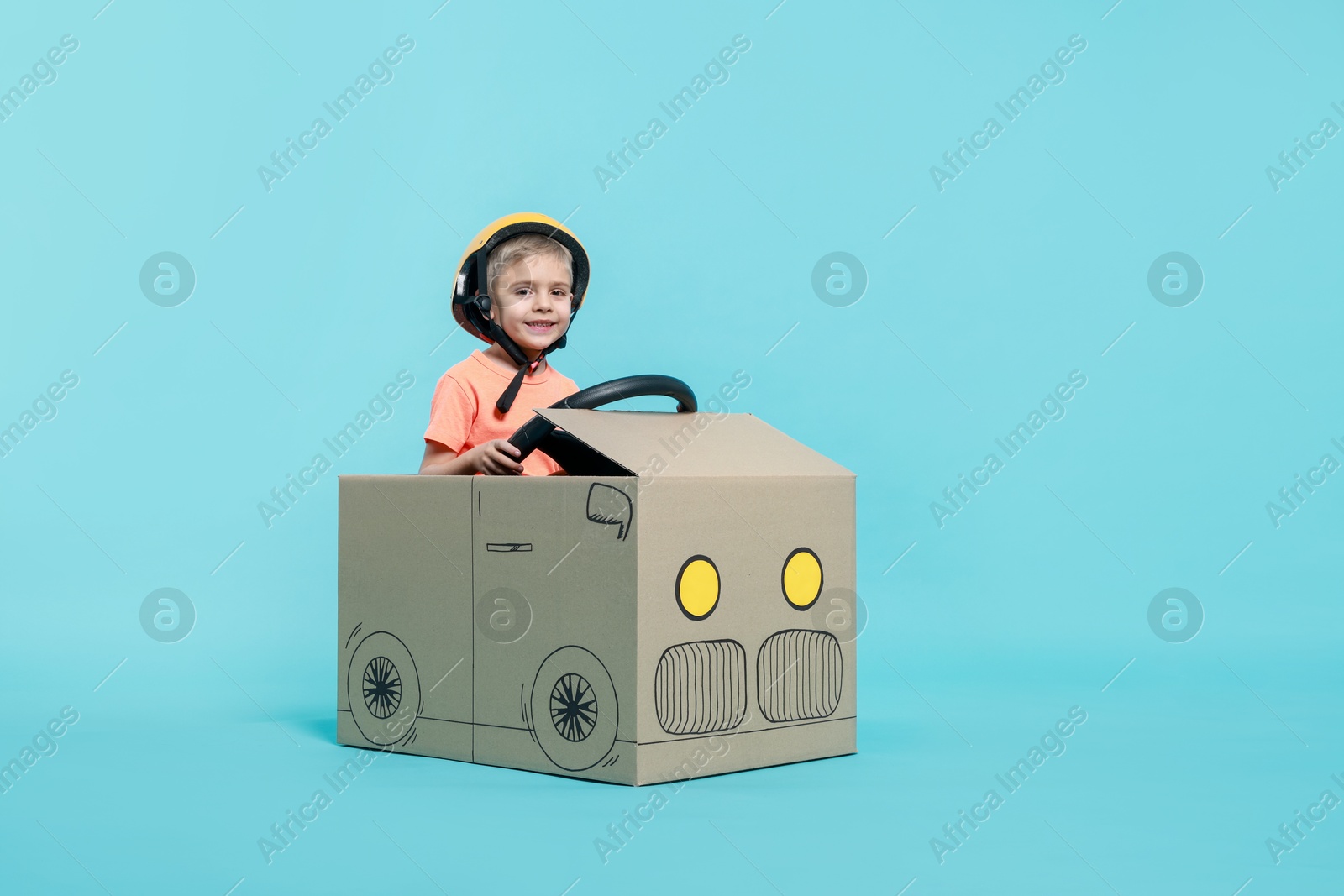 Photo of Little boy driving car made of cardboard on light blue background