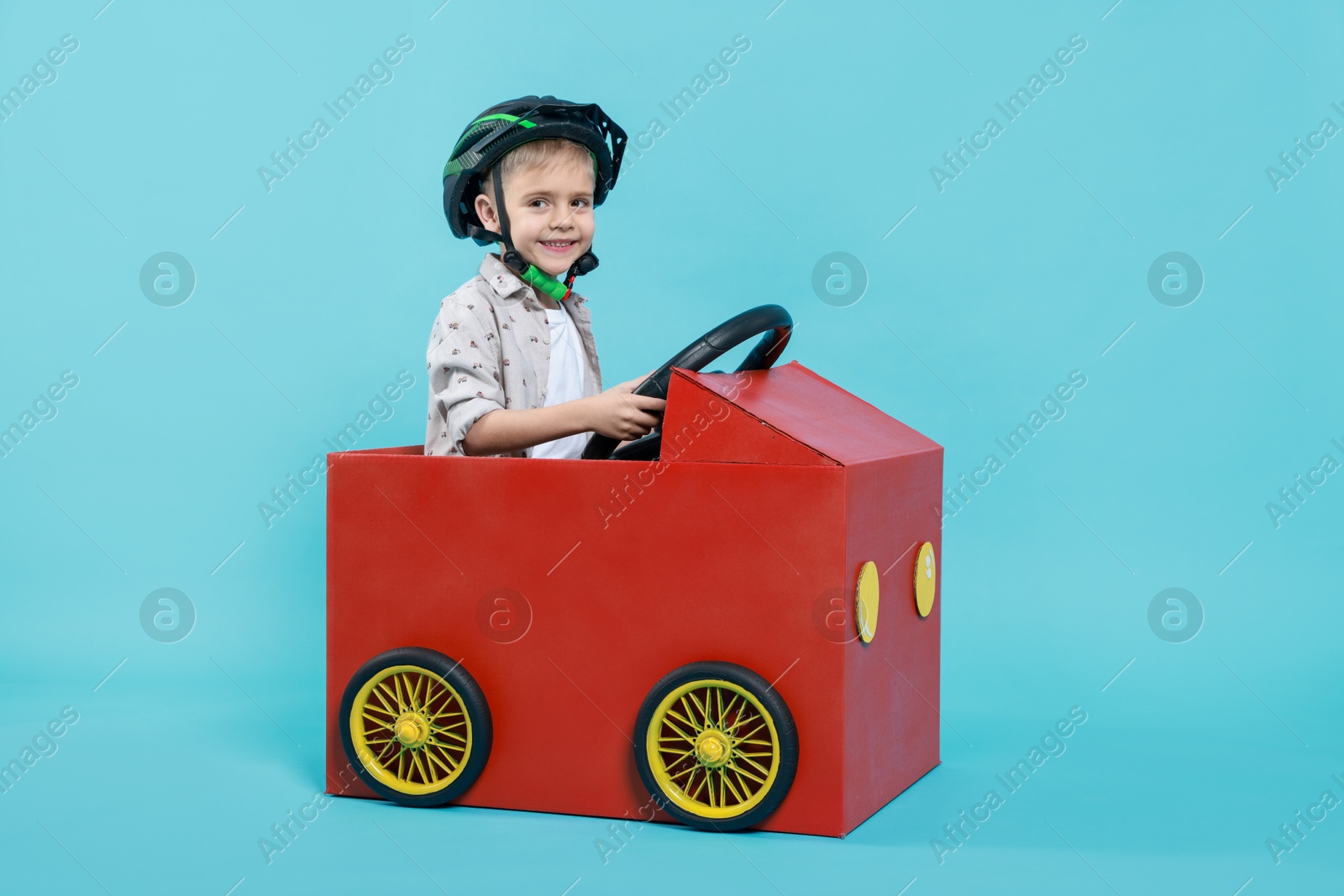 Photo of Little boy driving car made of cardboard on light blue background