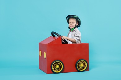 Photo of Little boy driving car made of cardboard on light blue background