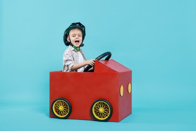 Photo of Little boy driving car made of cardboard on light blue background