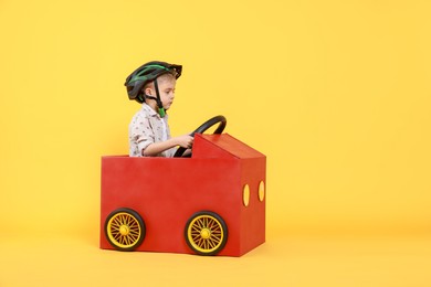 Photo of Little boy driving car made of cardboard on yellow background