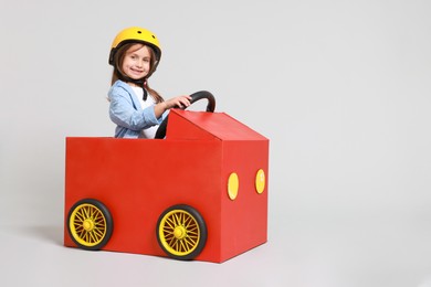 Photo of Little girl driving car made with cardboard on light background. Space for text