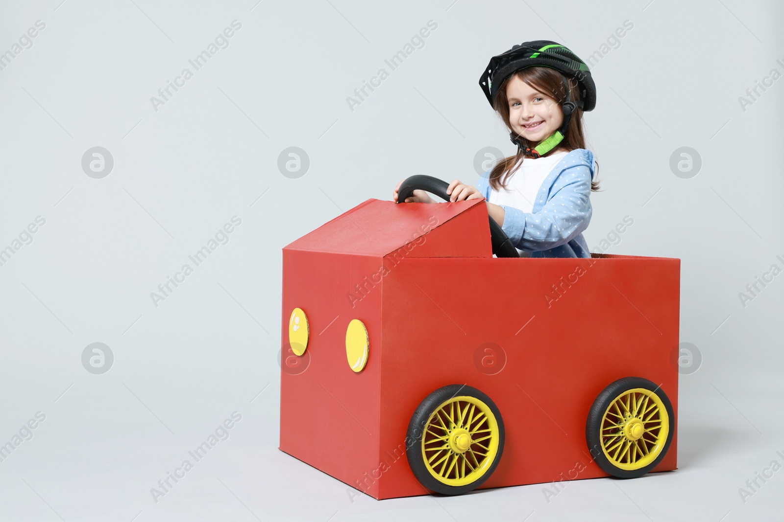 Photo of Little girl driving car made with cardboard on light background. Space for text