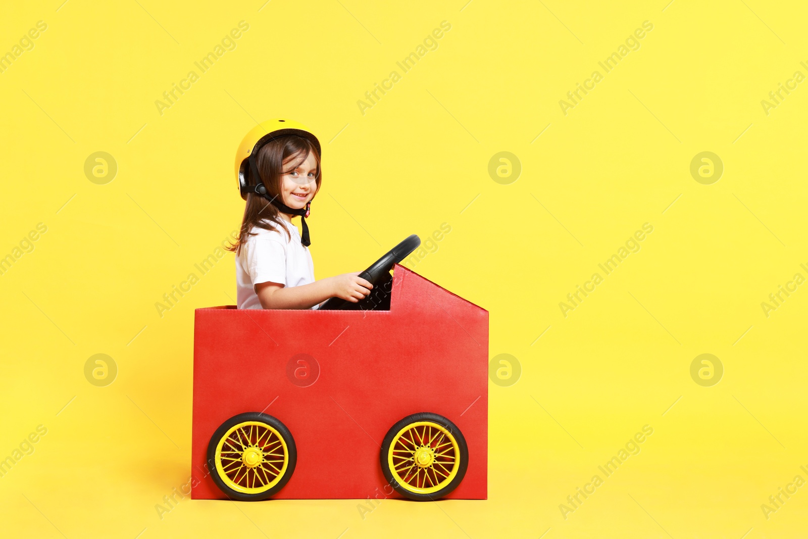 Photo of Little girl driving car made with cardboard on yellow background. Space for text