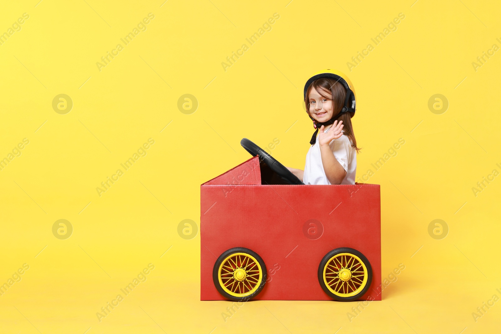 Photo of Little girl driving car made with cardboard on yellow background. Space for text