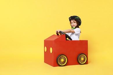 Photo of Little girl driving car made with cardboard on yellow background. Space for text