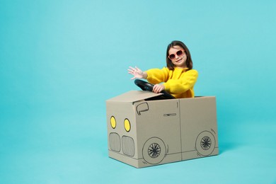 Photo of Little girl waving while driving car made with cardboard on light blue background. Space for text