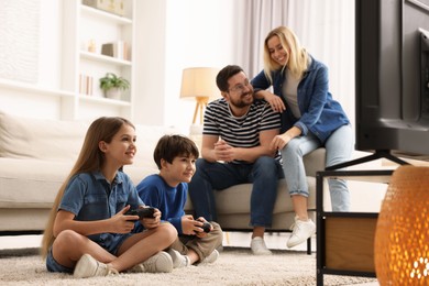 Photo of Cute kids playing video games while their parents resting on sofa at home, selective focus