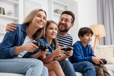 Photo of Happy family playing video games on sofa in living room