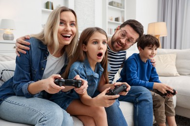 Photo of Happy family playing video games on sofa in living room