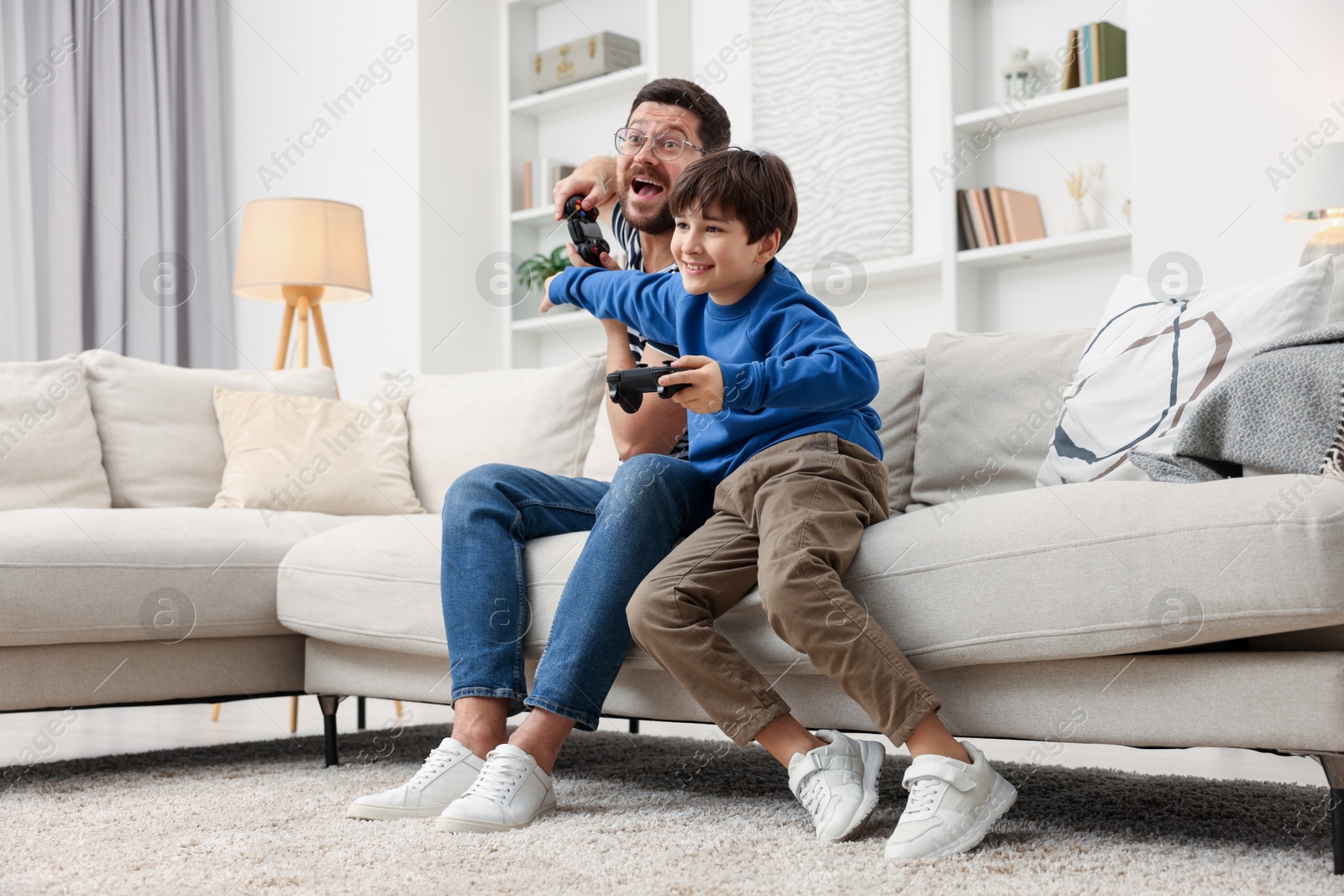 Photo of Father and his son playing video games on sofa in living room