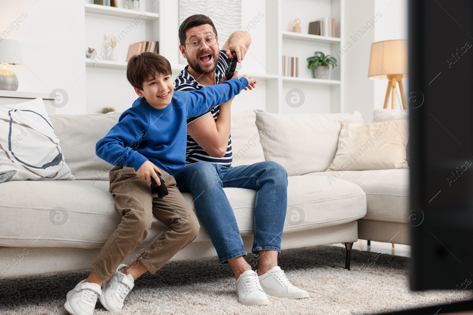 Photo of Father and his son playing video games on sofa in living room