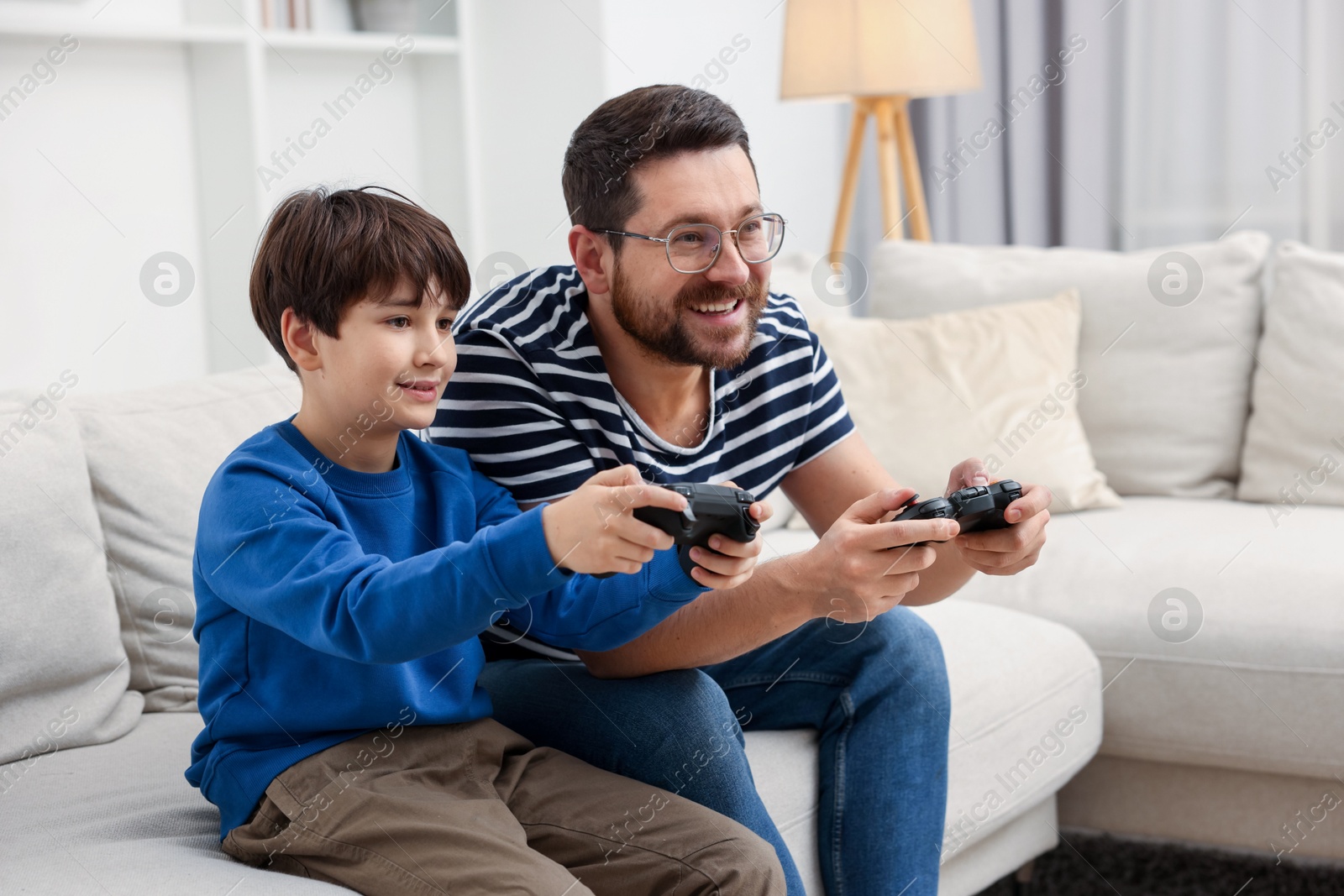 Photo of Father and his son playing video games on sofa in living room