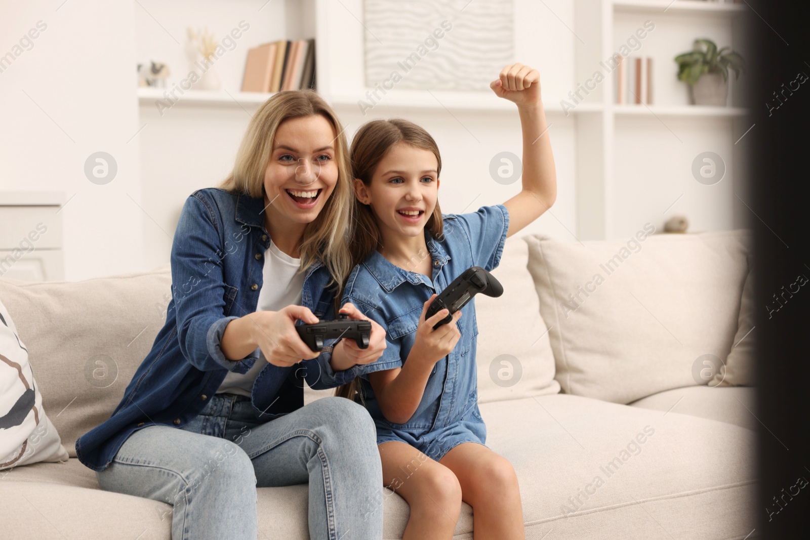 Photo of Happy mother and her daughter playing video games on sofa in living room