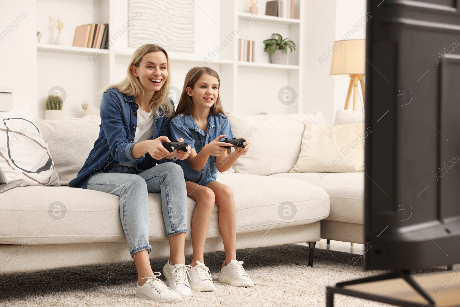 Photo of Happy mother and her daughter playing video games on sofa in living room