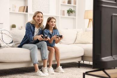 Photo of Happy mother and her daughter playing video games on sofa in living room