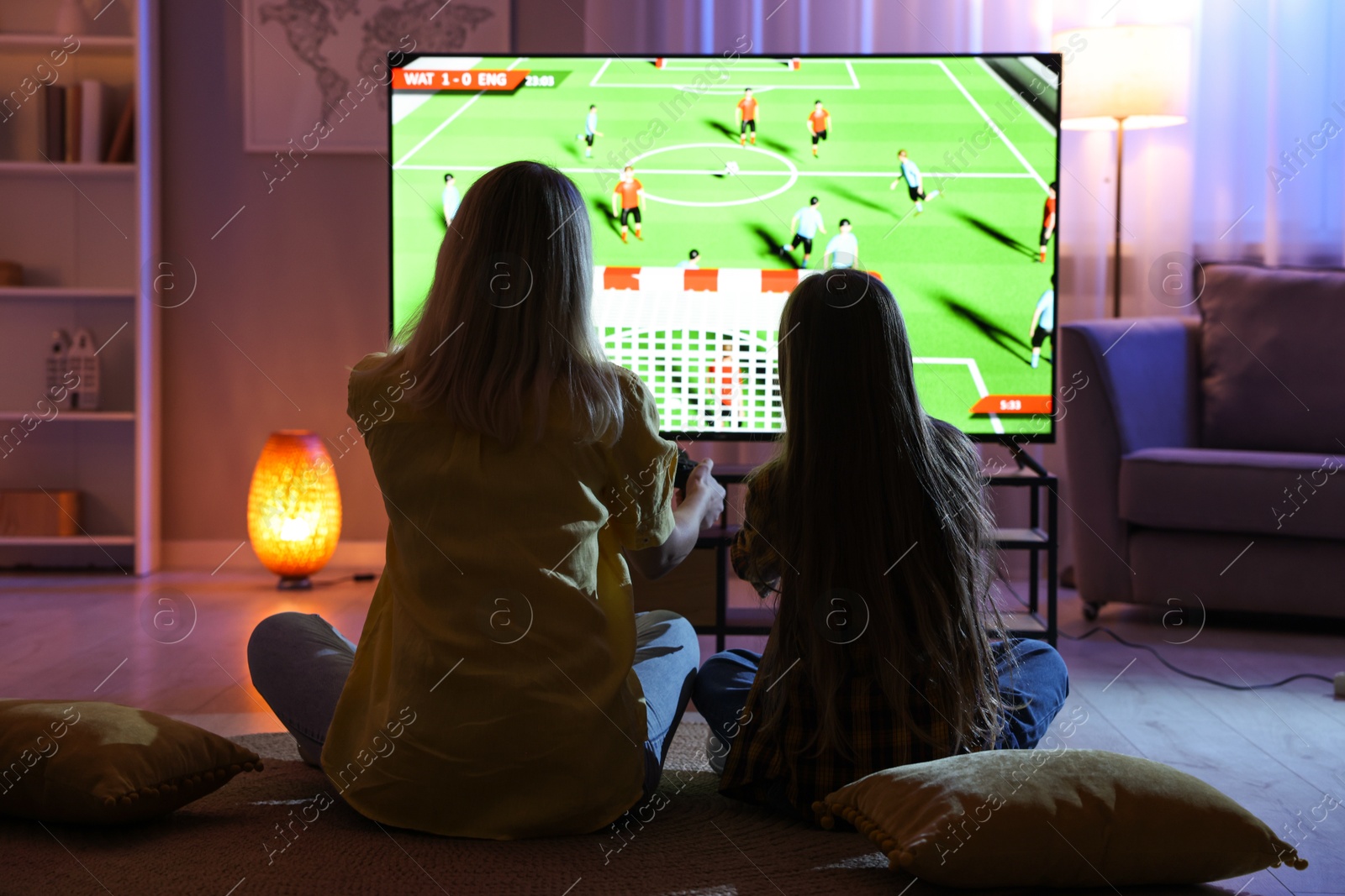 Photo of Mother and her daughter playing video game on floor in living room, back view