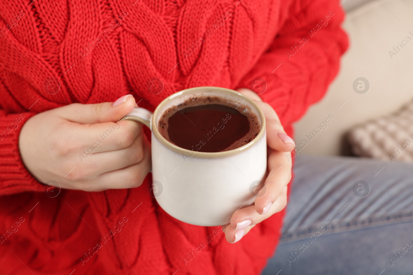 Photo of Woman holding mug of tasty hot chocolate on sofa, closeup