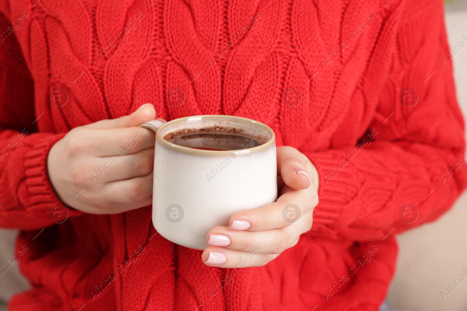 Photo of Woman holding mug of tasty hot chocolate on sofa, closeup