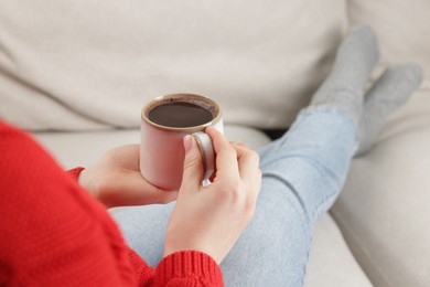 Photo of Woman holding mug of tasty hot chocolate on sofa, closeup