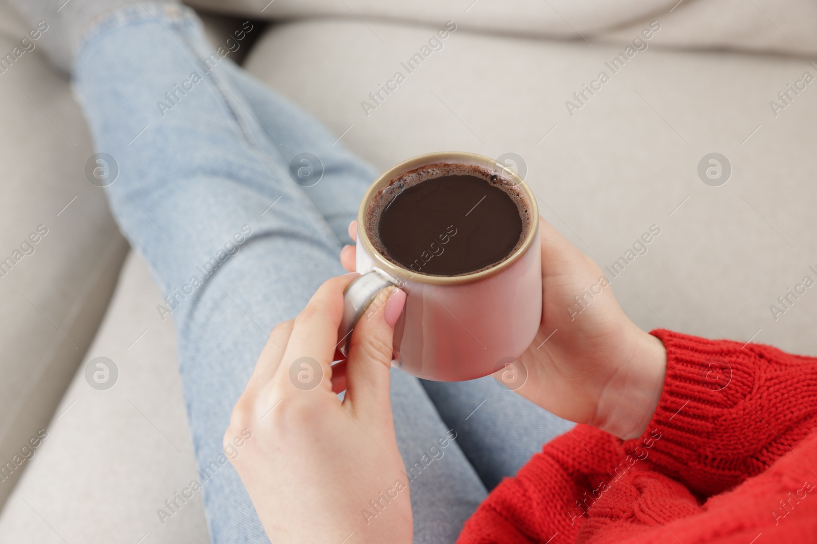 Photo of Woman holding mug of tasty hot chocolate on sofa, closeup