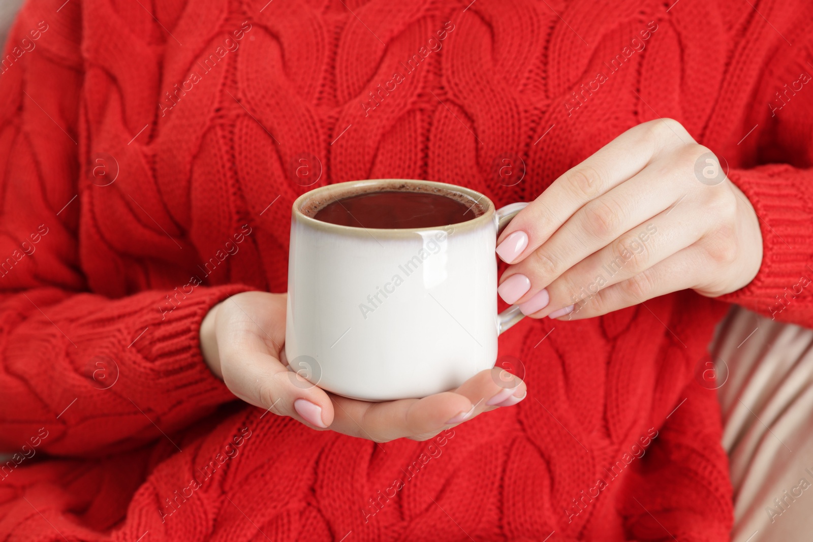 Photo of Woman holding mug of tasty hot chocolate on sofa, closeup