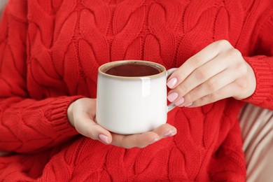 Photo of Woman holding mug of tasty hot chocolate on sofa, closeup