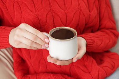 Photo of Woman holding mug of tasty hot chocolate on sofa, closeup