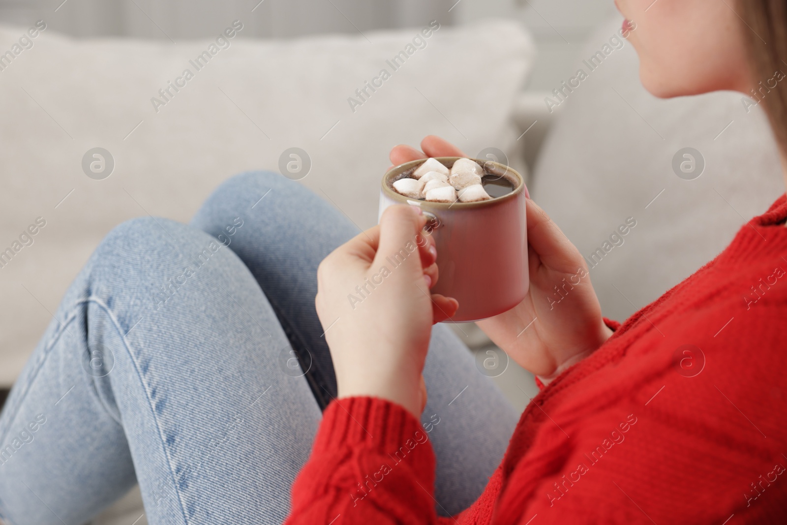 Photo of Woman holding mug of tasty hot chocolate with marshmallows on sofa, closeup