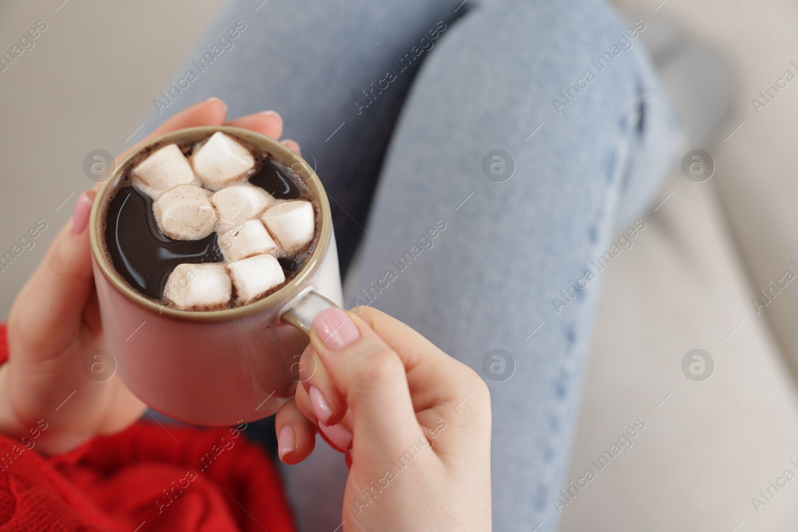 Photo of Woman holding mug of tasty hot chocolate with marshmallows on sofa, closeup