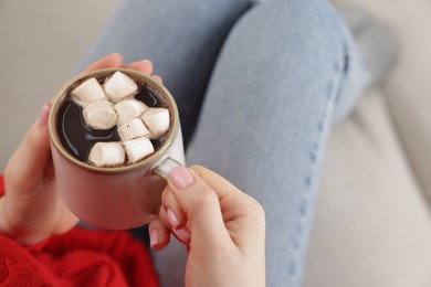 Photo of Woman holding mug of tasty hot chocolate with marshmallows on sofa, closeup