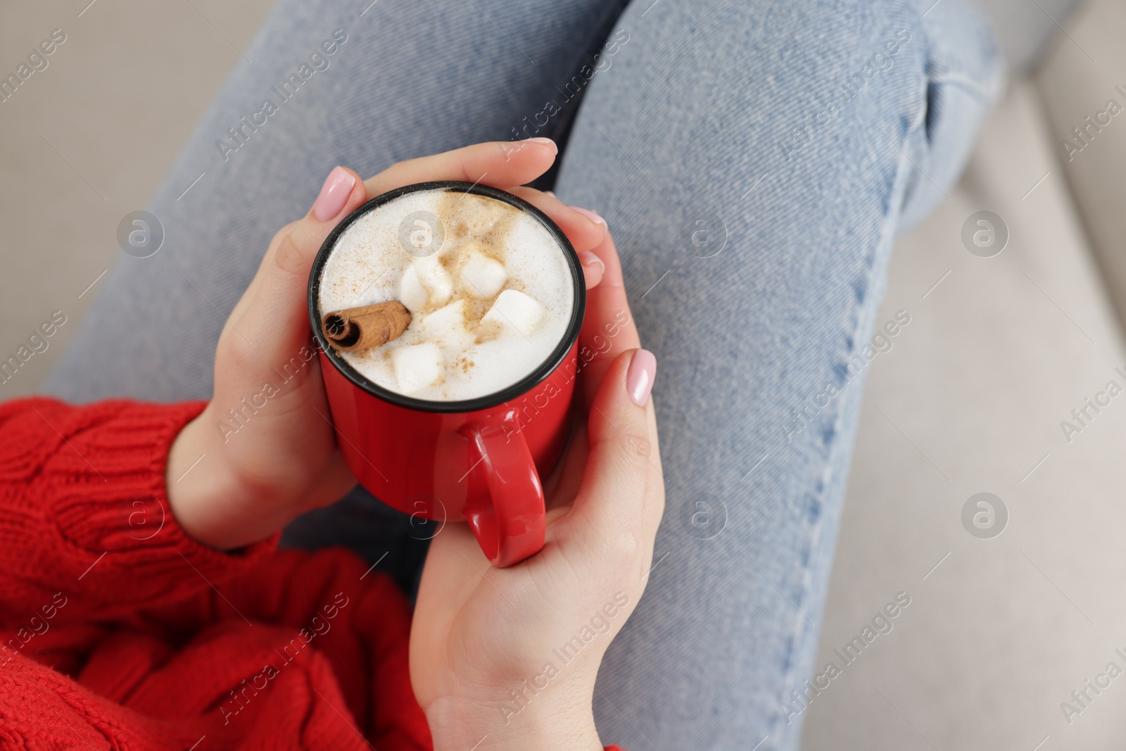 Photo of Woman holding mug of tasty hot chocolate with marshmallows on sofa, closeup