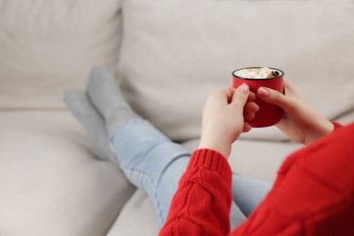 Photo of Woman holding mug of tasty hot chocolate with marshmallows on sofa, closeup. Space for text