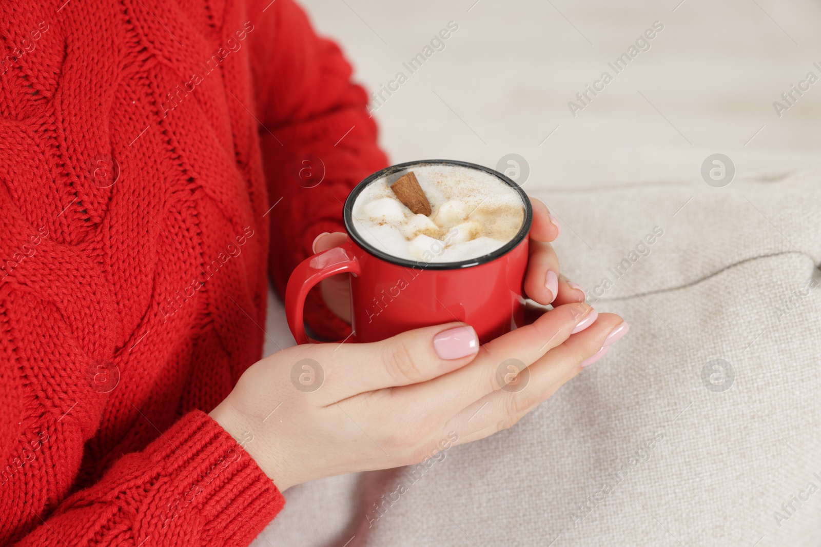 Photo of Woman holding mug of tasty hot chocolate with marshmallows on sofa, closeup