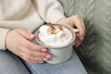 Photo of Woman holding mug of tasty hot chocolate with marshmallows and cinnamon, closeup