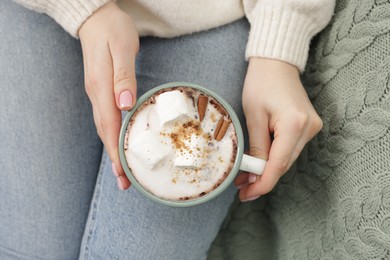 Photo of Woman holding mug of tasty hot chocolate with marshmallows and cinnamon, top view