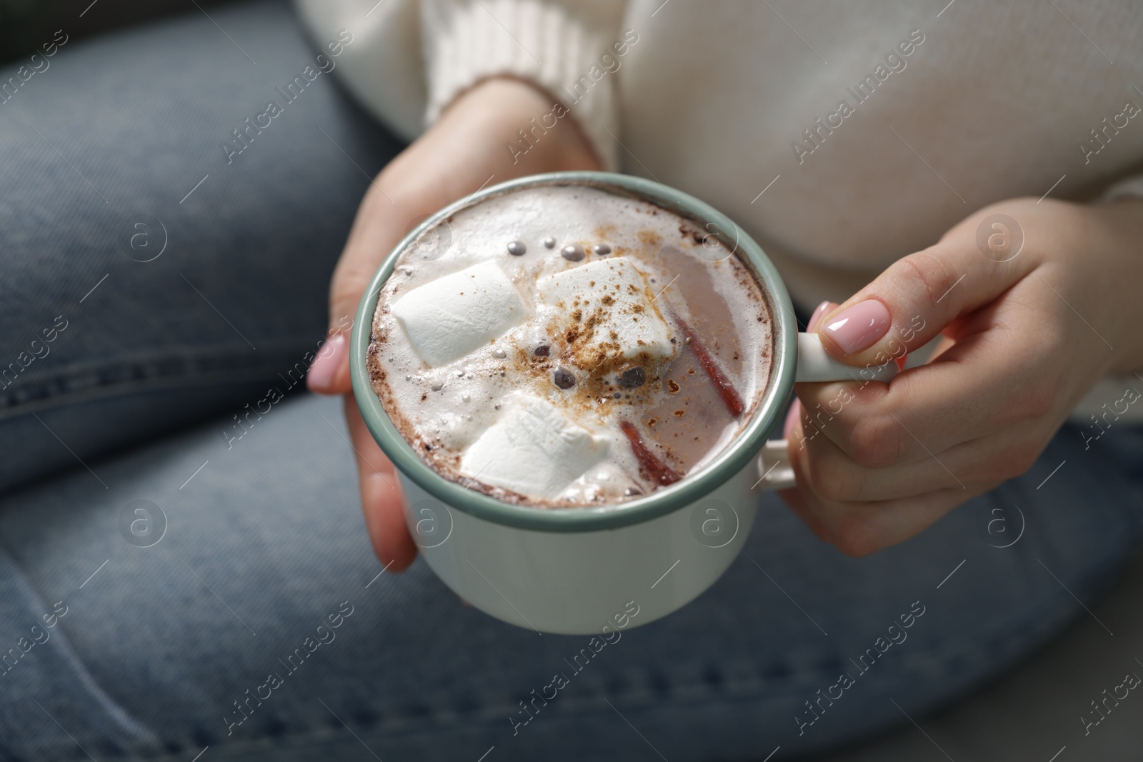 Photo of Woman holding mug of tasty hot chocolate with marshmallows and cinnamon on sofa, closeup