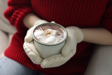 Photo of Woman holding mug of tasty hot chocolate with marshmallows and cinnamon on sofa, closeup