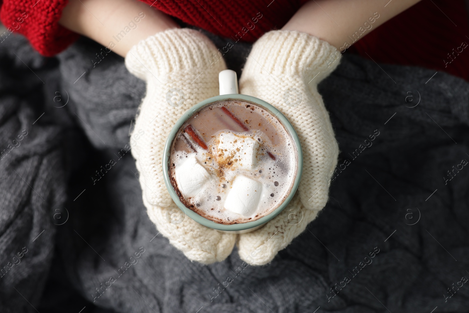 Photo of Woman holding mug of tasty hot chocolate with marshmallows and cinnamon, top view