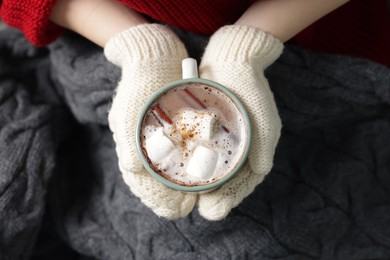 Photo of Woman holding mug of tasty hot chocolate with marshmallows and cinnamon, top view