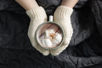 Photo of Woman holding mug of tasty hot chocolate with marshmallows and cinnamon, top view