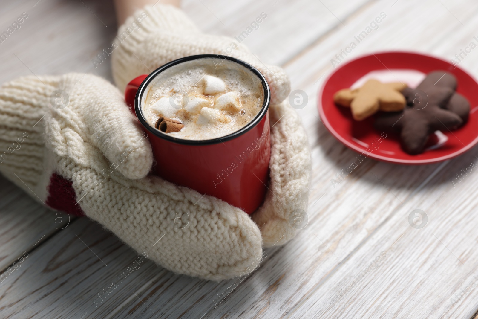 Photo of Woman having tasty hot chocolate with marshmallows, cinnamon and cookies at white wooden table, closeup