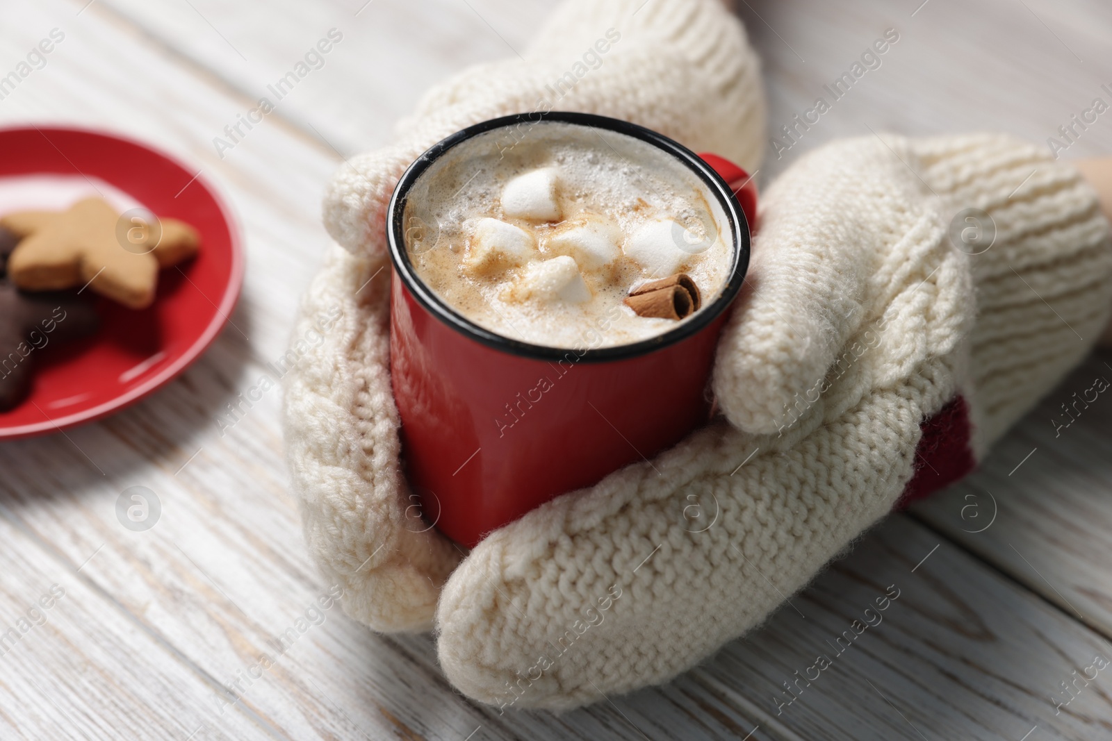 Photo of Woman having tasty hot chocolate with marshmallows, cinnamon and cookies at white wooden table, closeup