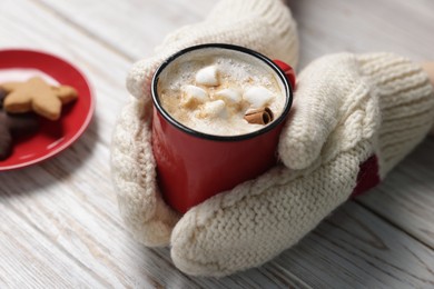 Photo of Woman having tasty hot chocolate with marshmallows, cinnamon and cookies at white wooden table, closeup