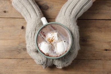 Photo of Woman holding mug of tasty hot chocolate with marshmallows at wooden table, top view