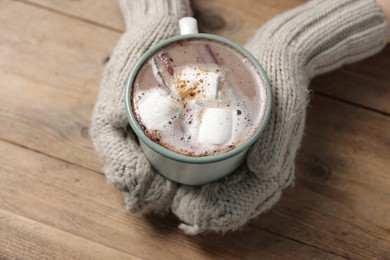 Photo of Woman holding mug of tasty hot chocolate with marshmallows at wooden table, closeup