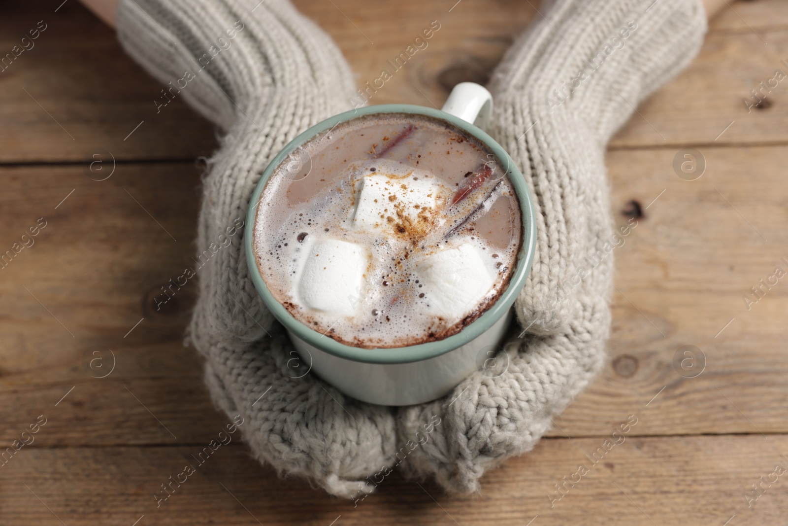 Photo of Woman holding mug of tasty hot chocolate with marshmallows at wooden table, closeup